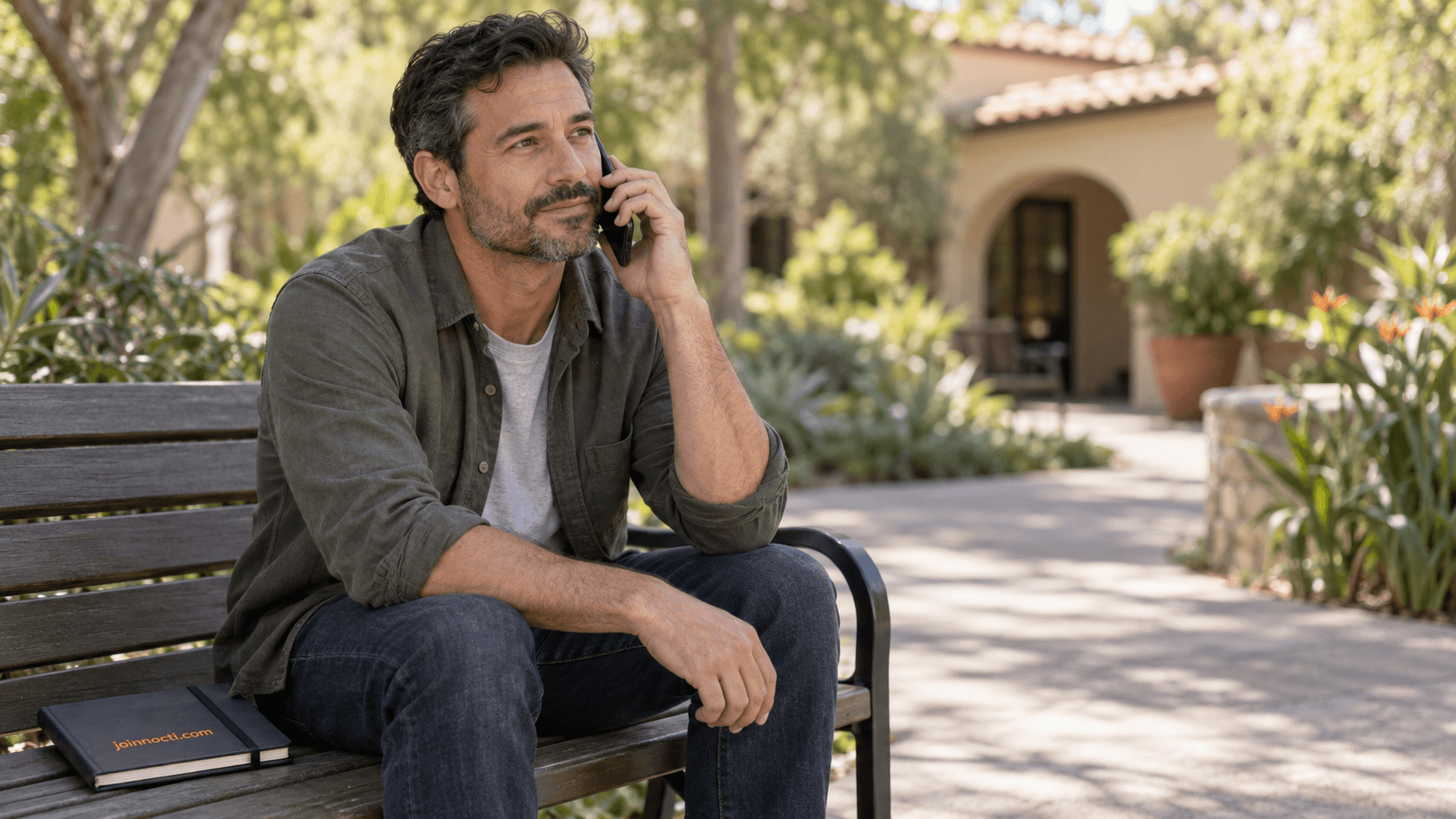 Adult man making a private support call on a quiet Southern California courtyard bench beside a NOCTI notebook