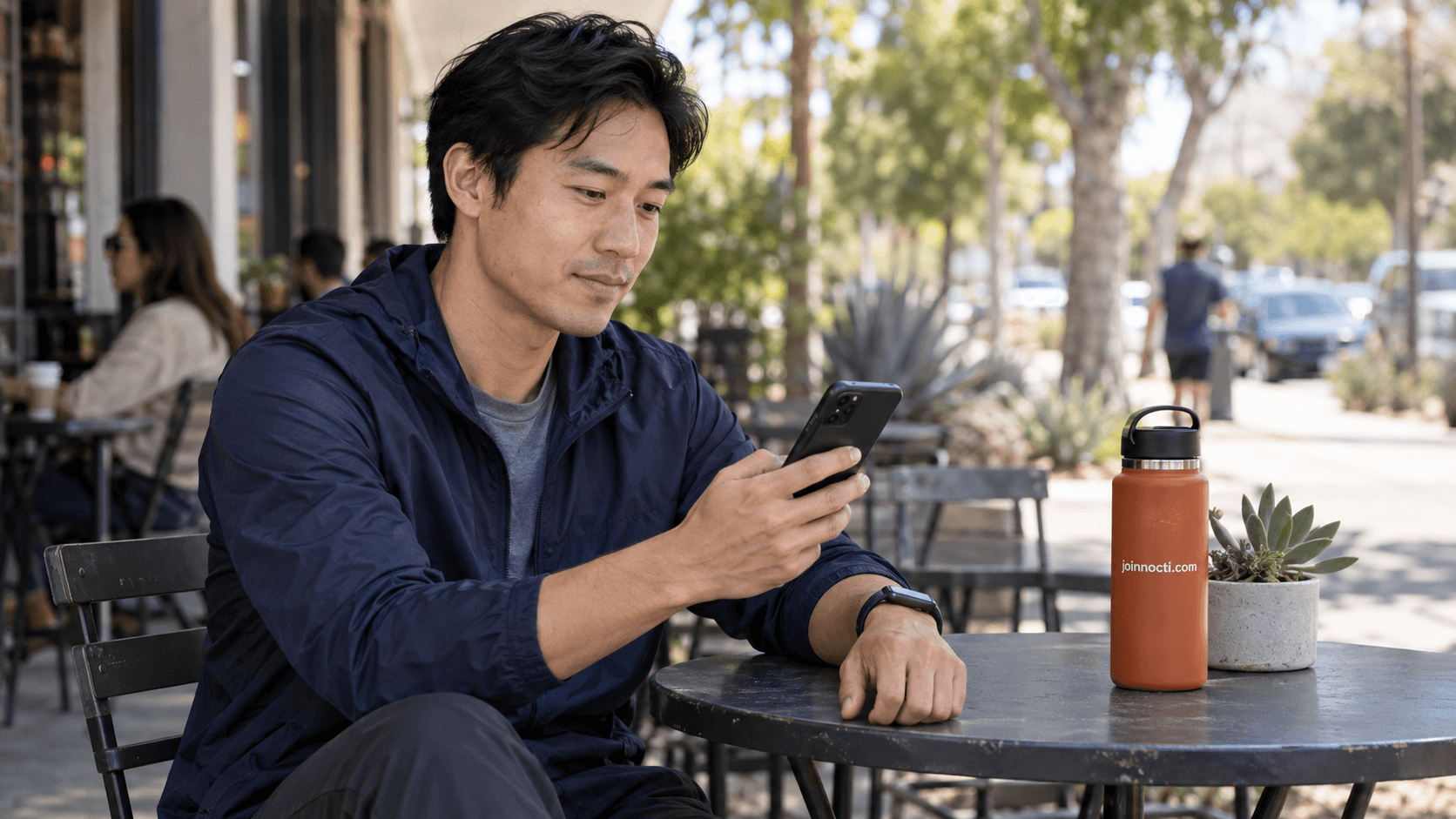 Man reviewing privacy settings on his phone while wearing a generic fitness tracker at a Southern California cafe patio