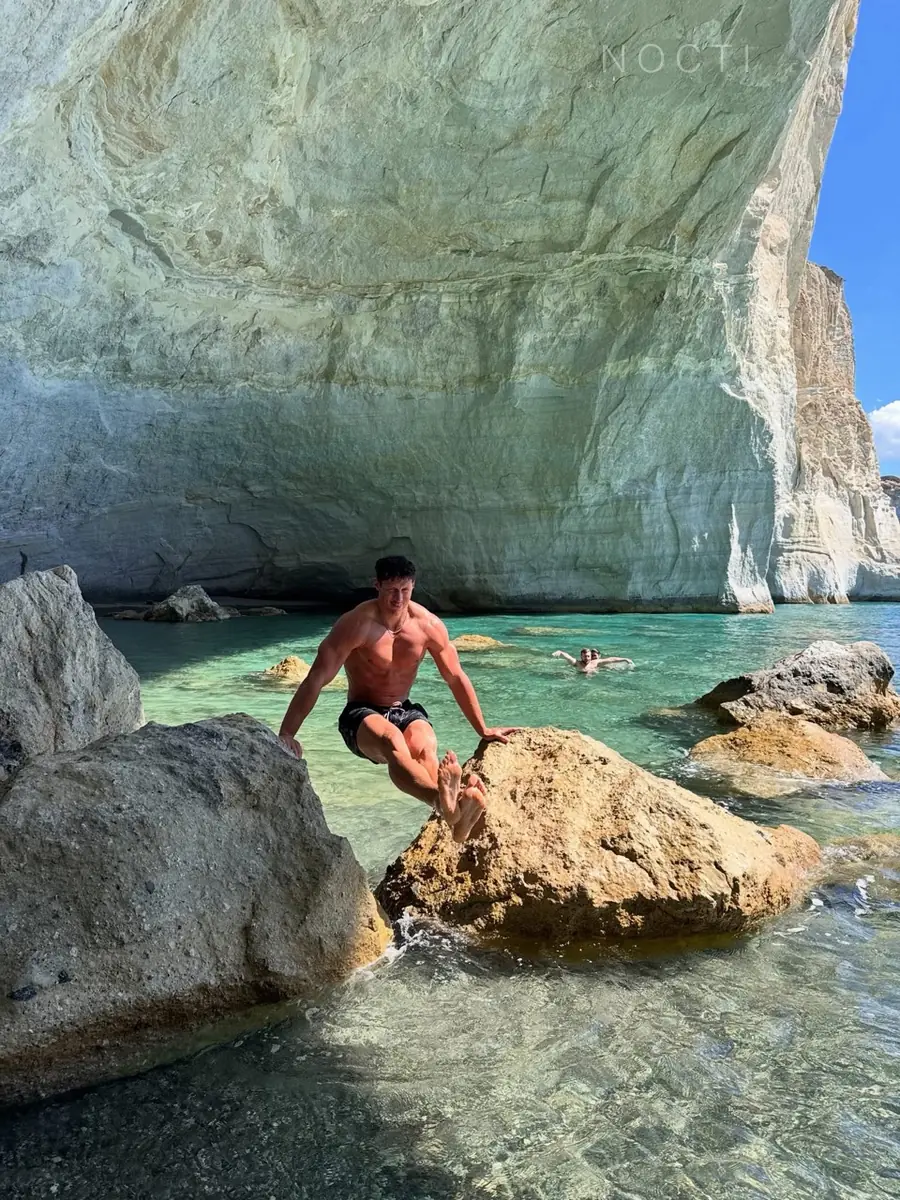 Adult male model balancing on coastal rocks beneath a subtle NOCTI mark, illustrating a sustainable physical practice