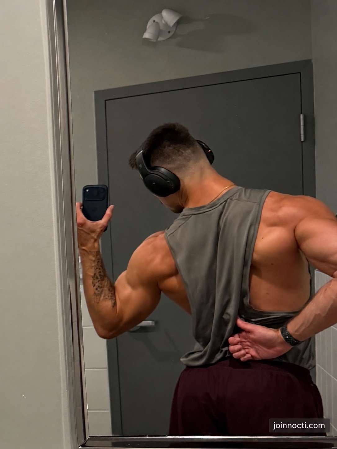 Philippe Milon photographs his back and shoulders in a gym mirror while wearing a gray training top